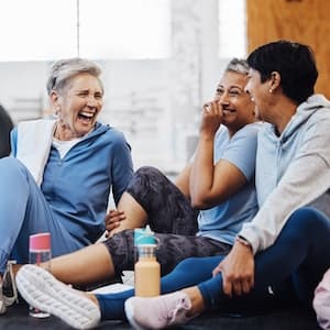 Three adults in workout clothes sit and laugh in a gym