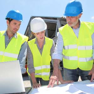 Three construction workers confer over plans, outdoors