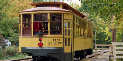 a restored historic streetcar rests on the tracks, surrounded by trees at a depot