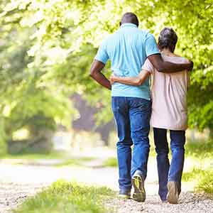 Elderly Black couple walking down a forested path, embracing