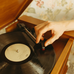 A person's hand steadies a phonograph needle before placing it on a record 