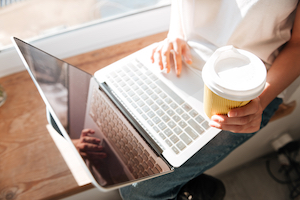 Woman's hands holding coffee cup and working on laptop