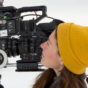 Tasha Van Zandt looks through a video camera lens, standing on frozen ocean