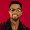 C Terrence Anderson wears a red and black plaid jacket over a gray shirt. He is Black, wears glasses, and has a short goatee.