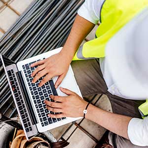 A construction worker types on a laptop on the jobsite.