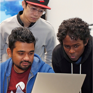 Three international graduate students lean down to look at a computer screen