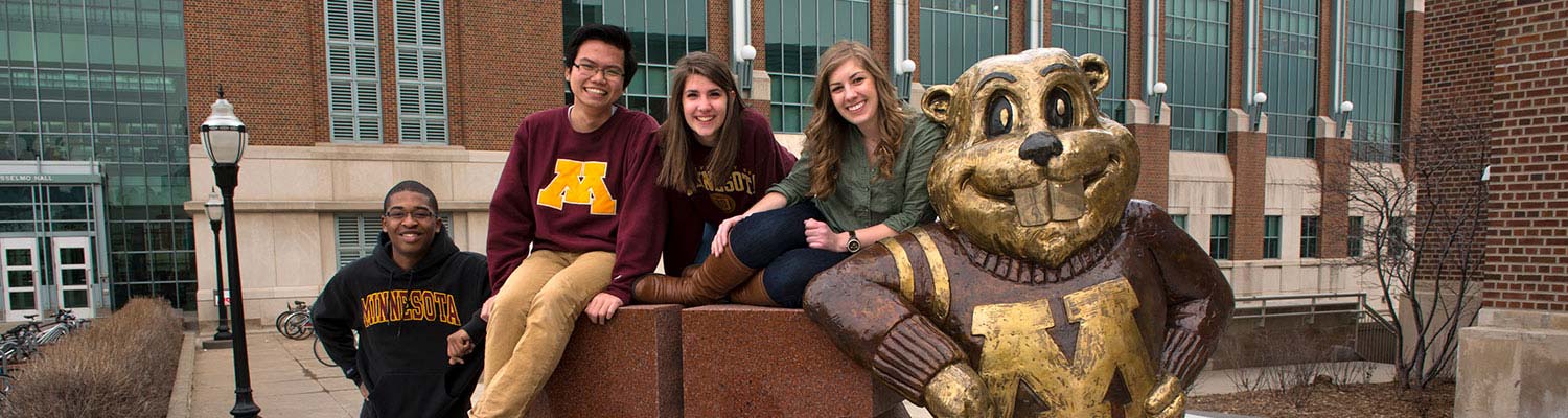 Four students lean on the Goldy statue outisde Coffman Union