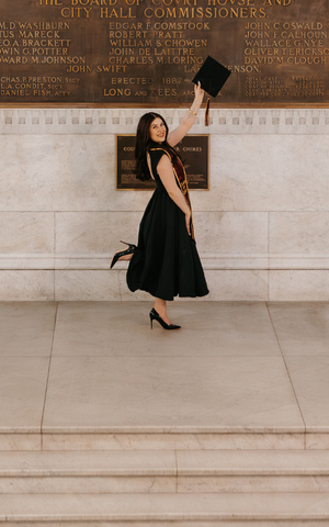 Ellexa Orbeck holds her commencement cap high while celebrating on a marble staircase