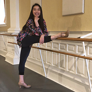Ashley Chin-Mark stands with her leg on the balance bar, elbow on knee, hand to chin