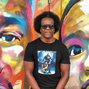 Willie Austin leans against a wall with a brightly-colored mural of two faces