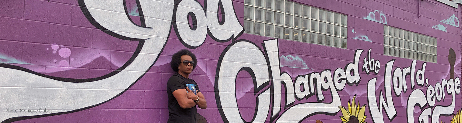 Willie Austin leans against a wall with mural that reads "You Changed the World,George"