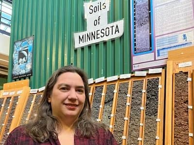 Hilary Major sits in front of a vertical display of soils samples from Minnesota