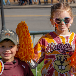 Two children decked out in maroon and gold hold a Goldy Gopher cutout sign and pom poms
