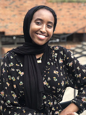 An East African woman wearing a dark headscarf with a big beautiful smile looks directly at camera
