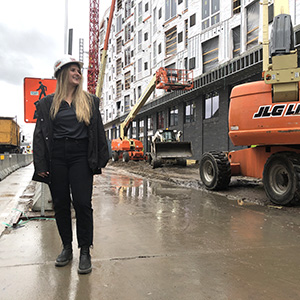 Cami Vargo stands in front of an apartment building under construction looking away from the camera