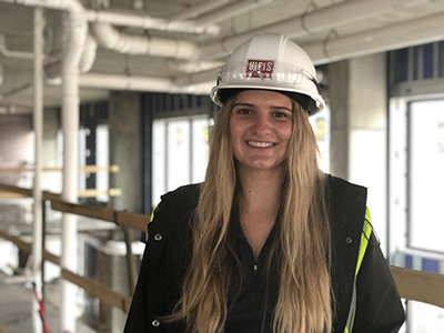 Cami Vargo stands in an apartment building under construction pipes and open walls in background