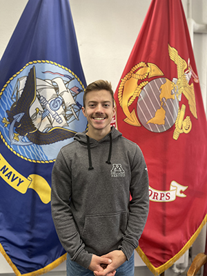 Owen Benson stands in front of two Navy flags