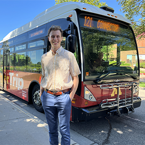 Luke Treiber stands in front of a U of M maroon and gold campus bus
