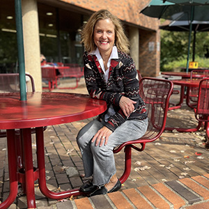 Beth Lory sits leaning forward at a maroon metal table in front of the Student Center on the U of M St. Paul campus
