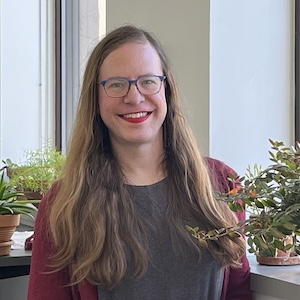 Kat Rohn stands in front of a windowsill filled with plants in their office at OutFront Minnesota