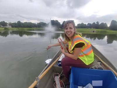 Kristin Seaman sits in a boat on a small pond with a fountain in the background