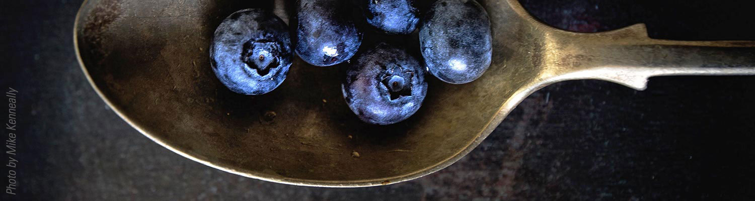 An antique spoon full of blueberries on dark background.