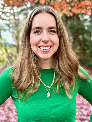Liz Hruska headshot wearing green long-sleeved shirt with golden fall leaves in background