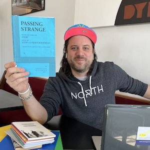 Lucas Erickson holds up a copy of the play Passing Strange as he sits at a table in a coffeeshop