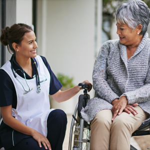 A nurse kneels to engage in conversation with a woman sitting in a wheelchair
