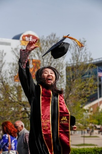 A graduate tosses her mortarboard into the air.