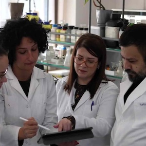 Three scientists in white lab coats look at a tablet