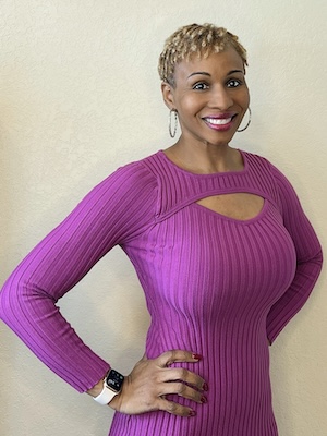 Shaun Telepak, a Black woman with short blond hair, stands with her hands on her hips. She is wearing a fucshia dress and large hoop earrings.