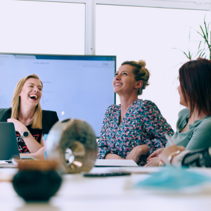 A group of professional women sit around a conference table laughing
