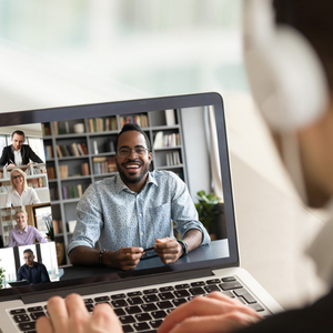A person seen from behind wearing white earphones engages in a virtual team meeting happening via their laptop