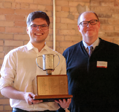 Zeke Jackson holds the Tomato Can Loving Cup Award while standing next to Vladas Griskevicius, Associate Dean of the Carlson Undergraduate Program 