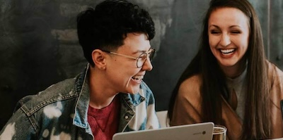 Two people laugh while working on laptops