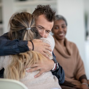 A man and a woman hug while a counselor looks on.