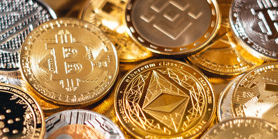 A pile of gold-tone coins bearing the logos of various cryptocurrencies.