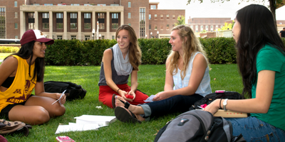 Four femaile students sit on the Northrop lawn conversing