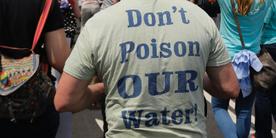 The back of a protester's shirt, reading "Don't Poison OUR Water!"