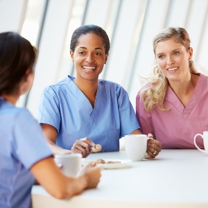 Three women in medical scrubs sit at a conference table