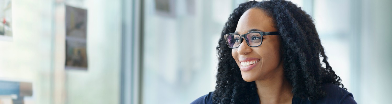 Black woman sitting at office desk, smiling, looking out window