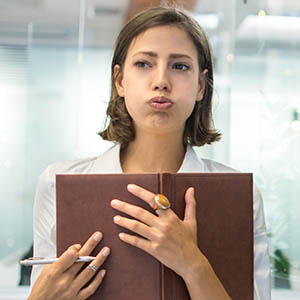 White professional looking stressed, carrying a notebook, in a bright office