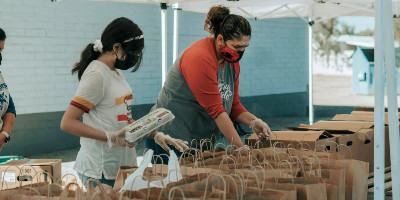 Volunteers load food into a table of paper bags