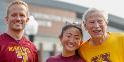 Three U of M alums from three different generations, smile outside Huntington Bank Stadium