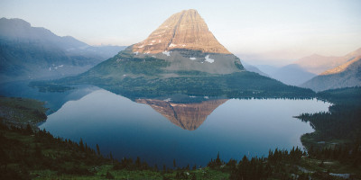 the peak of a sole mountain rises above a placid lake whose shores are wooded in pine