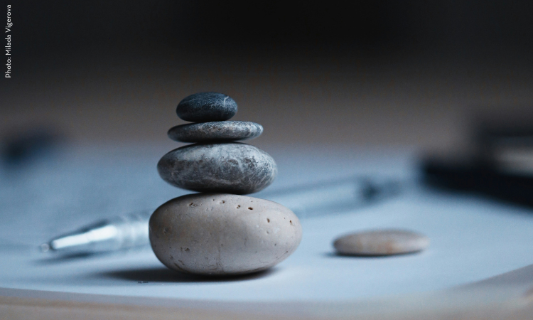 Four stones are stacked one on top of another on a desk that also contains a smaller stone and a pen 