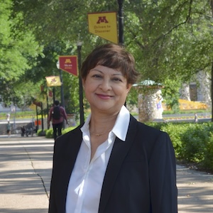 Dean Radhika Seshan on the mall sidewalk with maroon and gold flags in the background