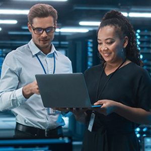 A man and woman stand in a data center looking at a laptop
