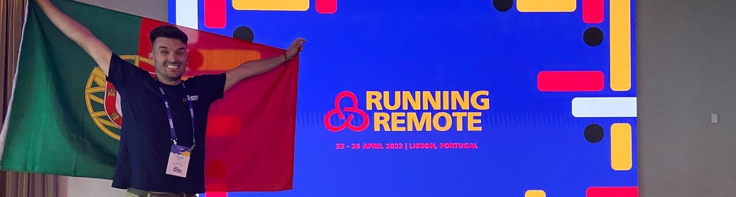 Forest Hall holds up a Portuguese flag in front of a sign for the Running Remote Conference in Lisbon.